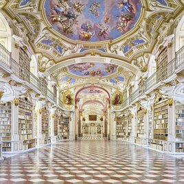 Prächtiger Bibliothekssaal des Stiftes Admont mit reich verziertem Deckenfresko, weißen Bücherregalen, goldenen Details und marmoriertem Boden in barocker Architektur.