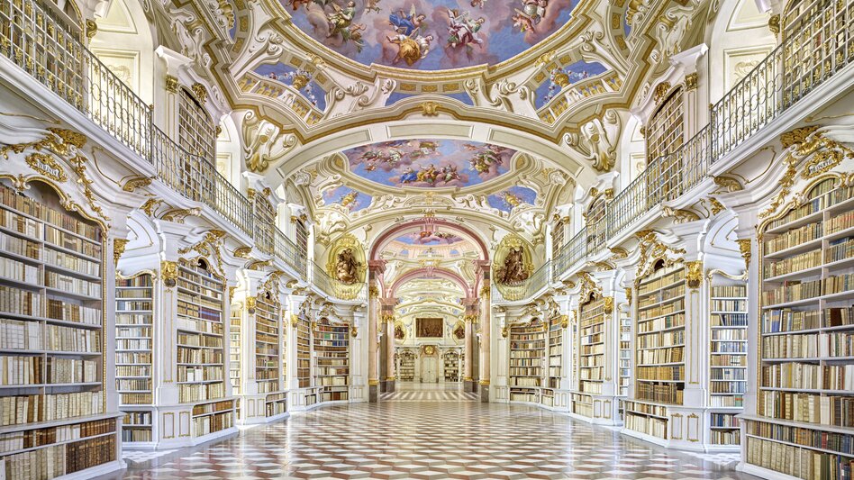 Prächtiger Bibliothekssaal des Stiftes Admont mit reich verziertem Deckenfresko, weißen Bücherregalen, goldenen Details und marmoriertem Boden in barocker Architektur.