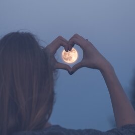 Eine Dame zeigt eine Hand in Herzform vor den Vollmond