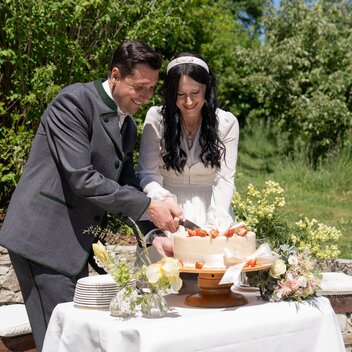 Das Brautpaar schneidet gemeinsam die Hochzeitstorte im Garten an. | © STG | Miriam Defregger