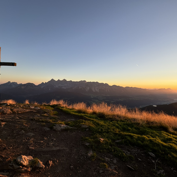 Gipfelkreuz auf der Reiteralm im goldenen Sonnenaufgang, mit weitem Blick auf das Dachsteinmassiv.