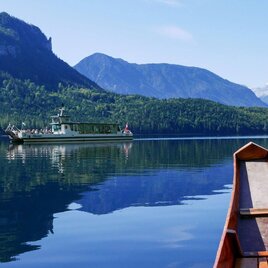 Ein ruhiger See umgeben von grünen Bergen. Ein Boot fährt sanft über die glatte Wasseroberfläche. | © Altaussee Schifffahrt