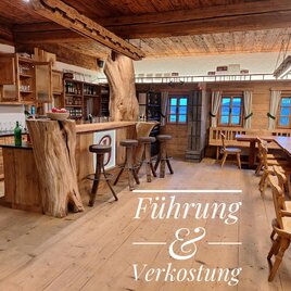 Eine gemütliche Bar aus Holz mit einem rustikalen Design. Im Hintergrund sind Tische und Stühle in einem einladenden Raum zu sehen. | © Hofladen Buchegger