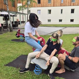 Eine Gruppe von Menschen bei einer Teambuilding Aufgabe von Raus in die Natur mit Jürgen Freller, welche sich mit verbundenen Augen auf einer Wippe im Freien bewegen. 
