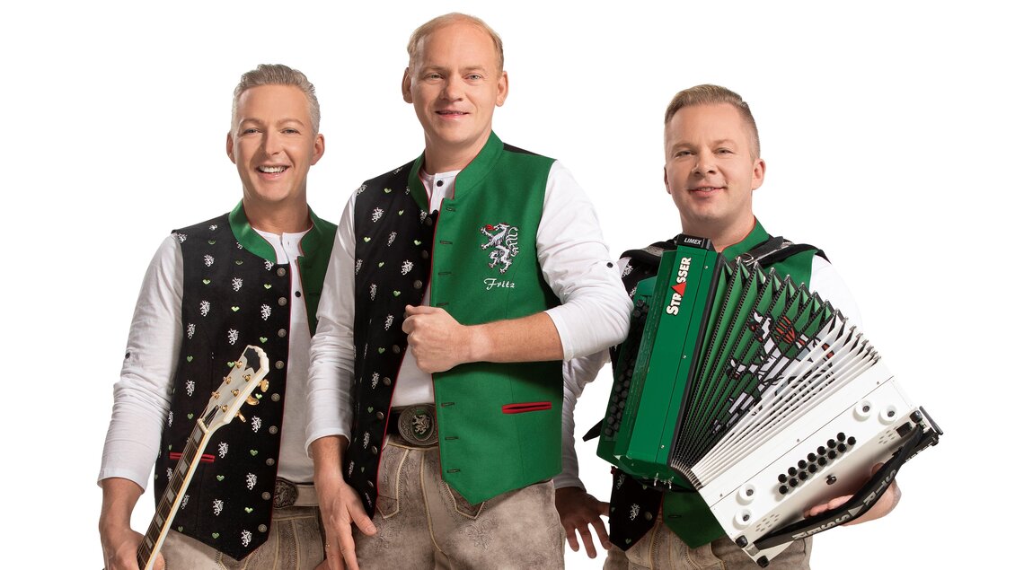 Eine Musikgruppe steht zusammen und lächelt. Sie tragen traditionelle Trachten und halten Instrumente in der Hand, darunter ein Akkordeon. | © DIE EDLSEER/Fotograf Karl Schrotter