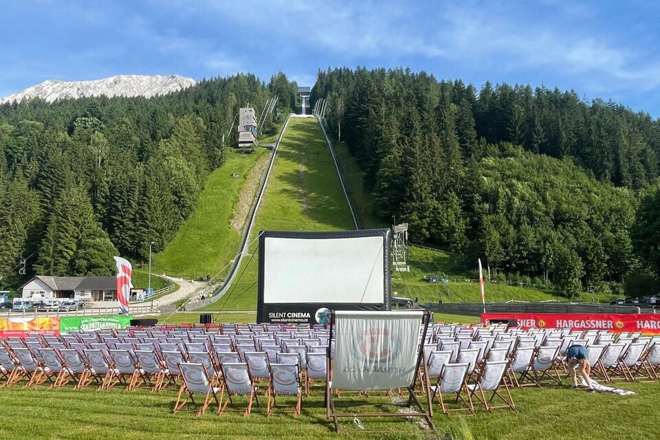 <p>Ein stimmungsvolles Freiluftkino an der Skiflugschanze Kulm mit gemütlichen Liegestühlen. Der Himmel im Hintergrund ist strahlend blau.</p> | © wirsindkulm