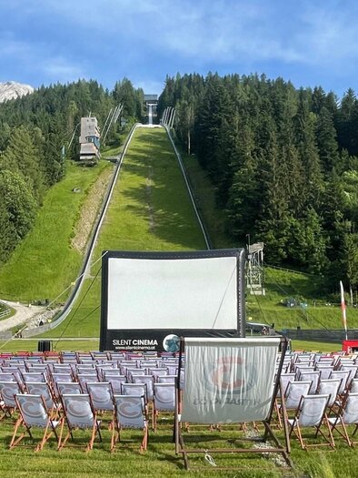 <p>Ein stimmungsvolles Freiluftkino an der Skiflugschanze Kulm mit gemütlichen Liegestühlen. Der Himmel im Hintergrund ist strahlend blau.</p> | © wirsindkulm