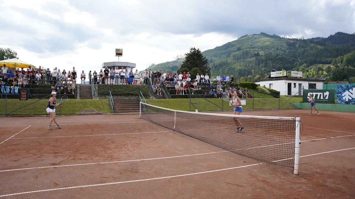 Zwei Spielerinnen spielen Tennis auf einem Sandplatz. Eine Gruppe von Zuschauern verfolgt das Spiel im Hintergrund. | © Stadt Bruck
