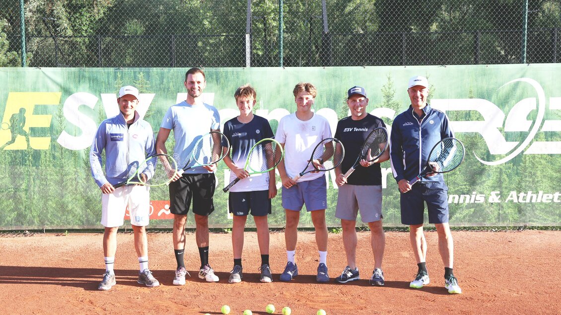 Sechs Männer stehen auf einem Tennisplatz und halten Schläger in der Hand. Im Hintergrund ist ein grünes Banner mit dem Logo einer Tennisschule zu sehen. | © Stadt Bruck