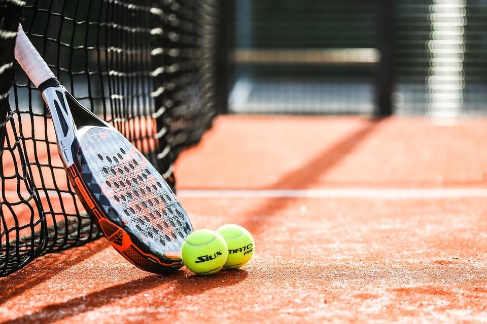 Ein Tennisnetz mit einem Schläger und zwei gelben Tennisbällen auf einem roten Platz. Der Schläger lehnt an dem Netz. | © pixabay.com