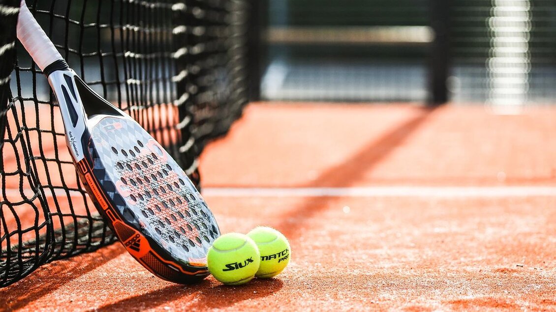 Ein Tennisnetz mit einem Schläger und zwei gelben Tennisbällen auf einem roten Platz. Der Schläger lehnt an dem Netz. | © pixabay.com