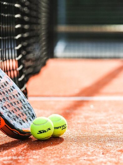 Ein Tennisnetz mit einem Schläger und zwei gelben Tennisbällen auf einem roten Platz. Der Schläger lehnt an dem Netz. | © pixabay.com