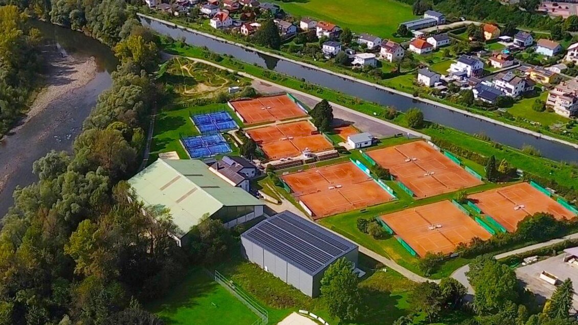 Eine tennis Anlage mit mehreren roten Sandplätzen und einem Sportgebäude. Im Hintergrund verläuft ein Fluss, umgeben von grüner Landschaft und Wohngebieten. | © ESV Bruck/Mur