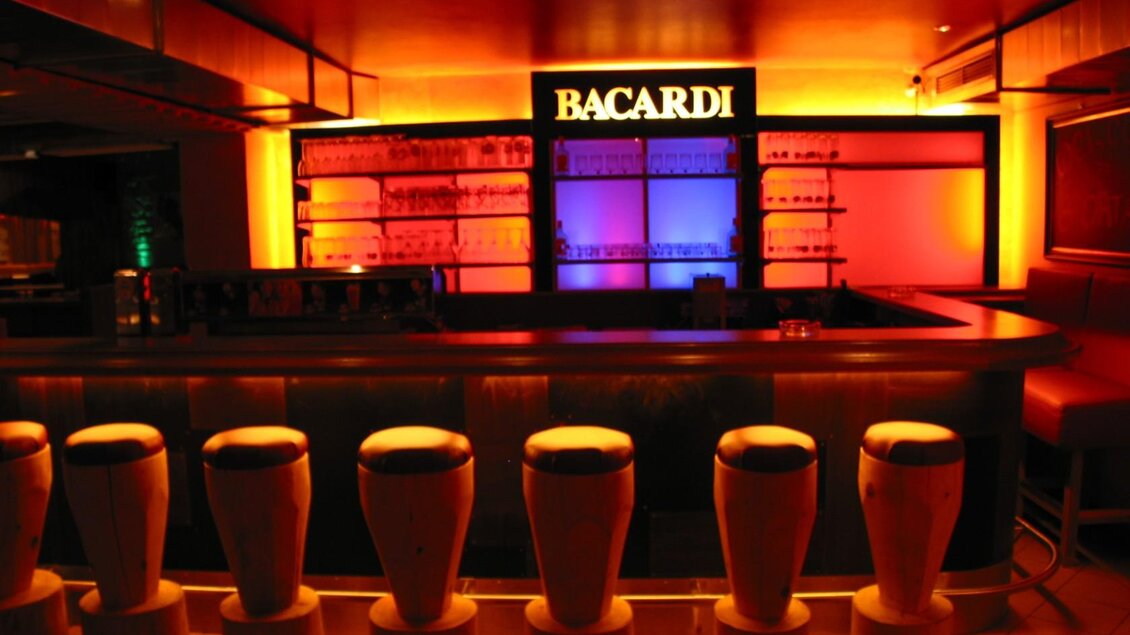 Eine stilvolle Bar mit beleuchteten Regalen und bunten Lichtern. Die Barstühle sind modern und einladend angeordnet. | © Hotel Seebacherhof