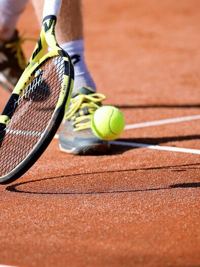 A tennis ball bounces on the court while a player hits it with a racket. The ground of the court is clearly visible. | © Pixabay