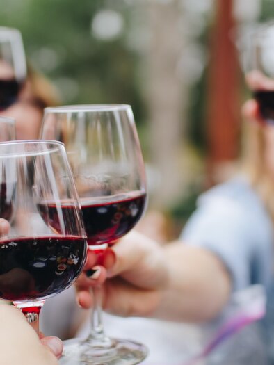 Eine Gruppe von Menschen stößt mit Gläsern Rotwein an. Die Atmosphäre ist festlich und fröhlich.