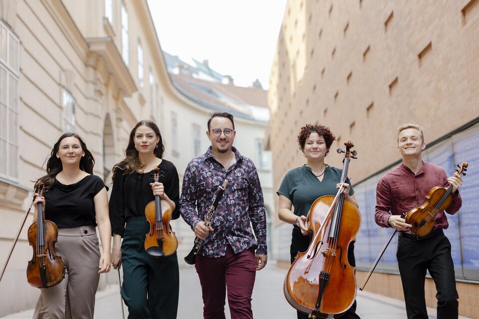 Drei Frauen sitzen auf einer Bank und lächeln. Neben ihnen liegt ein Cello auf dem Boden. | © Viktoria Hofmarcher