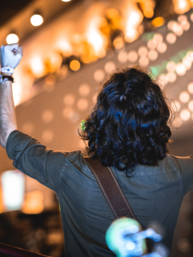 Musiker auf einer stimmungsvoll beleuchteten Bühne mit Gitarre, der die Arme begeistert in die Höhe streckt. Warme Lichter und farbenfrohe Bühneneffekte vermitteln ausgelassene Konzertstimmung und pure Freude an der Musik in Feldbach. | © Stadtgemeinde Feldbach