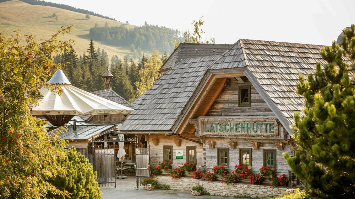 Eine malerische Berghütte mit einem schindelgedeckten Dach und bunten Blumen. Im Hintergrund sind sanfte Hügel und Bäume zu sehen. | © Tourismusverband Oststeiermark