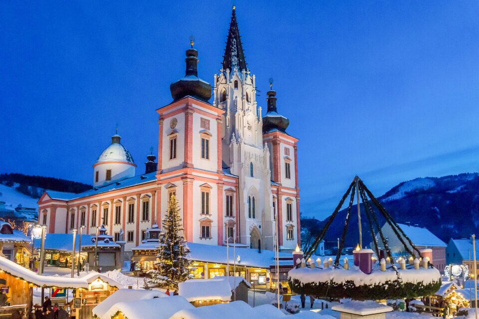 Eine beeindruckende Winteransicht eines Gebäudes mit einem hohen Turm. Der Platz ist festlich mit Weihnachtsmärkten und Lichtern geschmückt. | © Fred Lindmoser