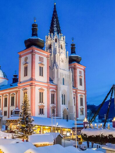 Eine beeindruckende Winteransicht eines Gebäudes mit einem hohen Turm. Der Platz ist festlich mit Weihnachtsmärkten und Lichtern geschmückt. | © Fred Lindmoser
