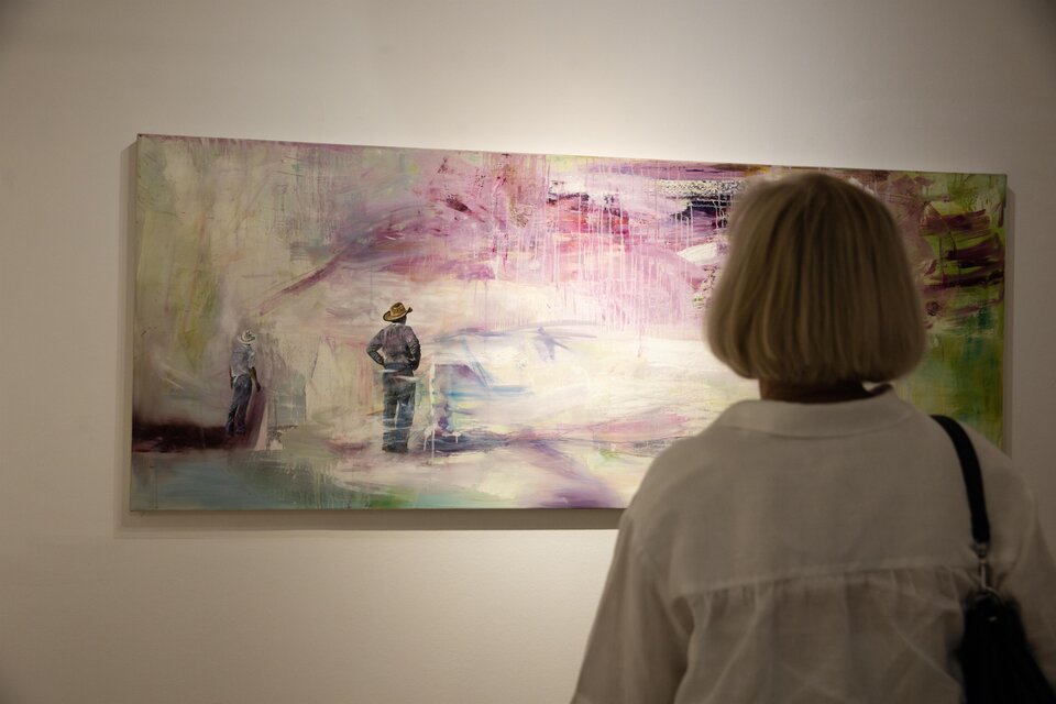 Eine Person betrachtet ein modernes Gemälde an einer Wand. Das Kunstwerk zeigt abstrakte Farben und Figuren. | © Achromatic Photography