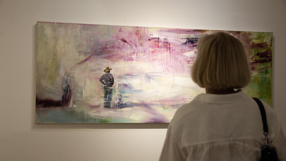 Eine Person betrachtet ein modernes Gemälde an einer Wand. Das Kunstwerk zeigt abstrakte Farben und Figuren. | © Achromatic Photography