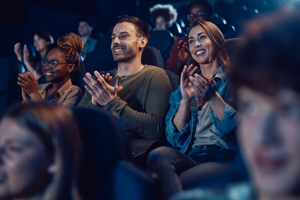 Eine Gruppe von Menschen sitzt in einem Kino und applaudiert. Sie wirken begeistert und genießen den Film. | © AdobeSTock