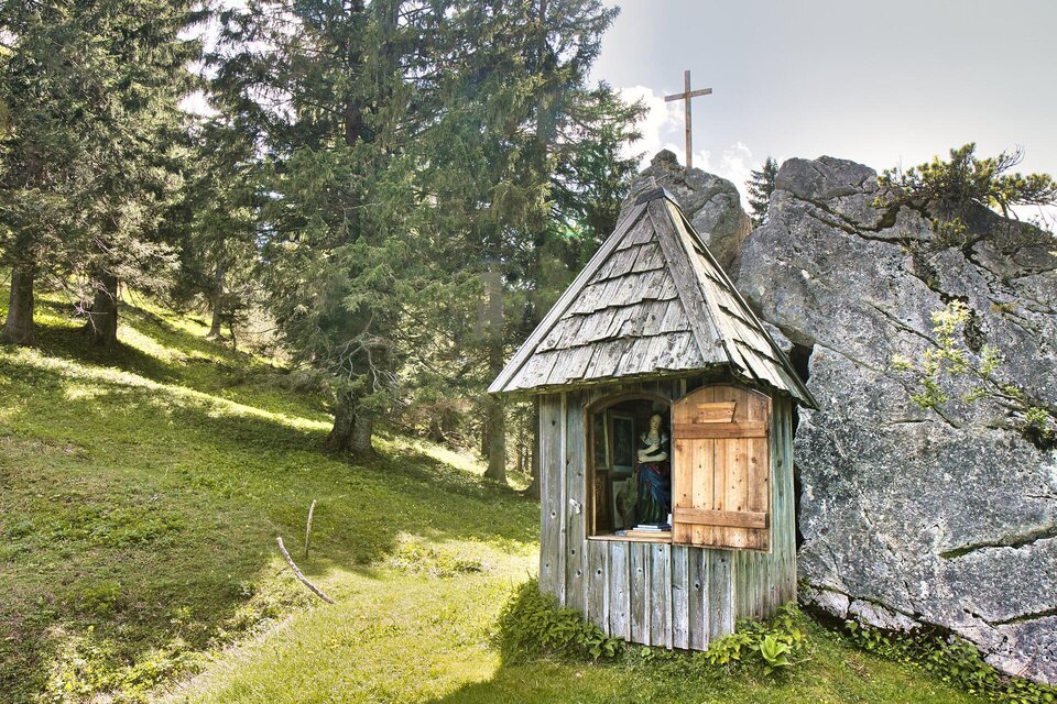 Eine kleine Holzkapelle steht zwischen Bäumen und Felsen. Im Hintergrund ist ein Kreuz zu sehen, das die ruhige Umgebung ergänzt. | © TV Gesäuse