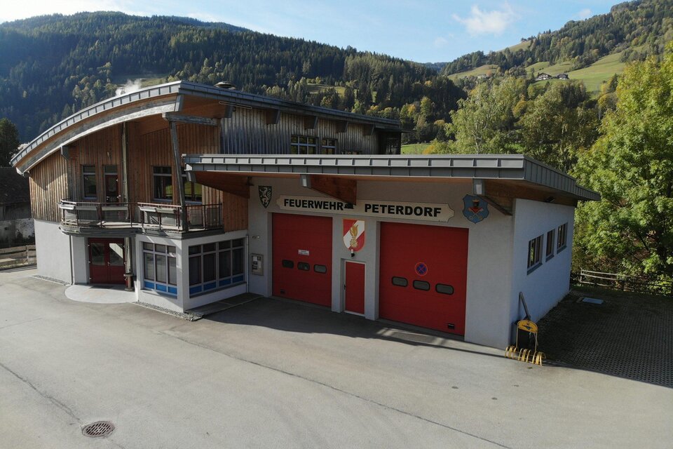 Ein modernes Feuerwehrhaus in der malerischen Umgebung von Peterdorf. Die rote Tore und die Holzkonstruktion verleihen dem Gebäude einen einladenden Eindruck.