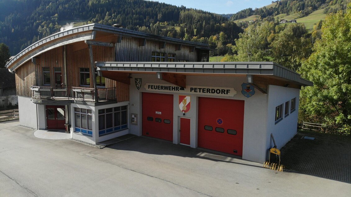 Ein modernes Feuerwehrhaus in der malerischen Umgebung von Peterdorf. Die rote Tore und die Holzkonstruktion verleihen dem Gebäude einen einladenden Eindruck.