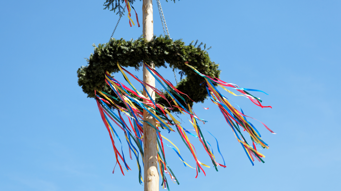 Ein geschmückter Maibaum mit bunten Bändern. Der Himmel ist klar und blau. | © Canva