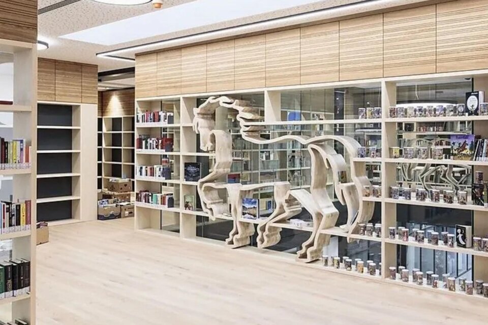 Heller Bibliotheksraum mit Bücherregalen und einer dekorativen Regalinstallation in Form eines Pferdes, in der Bibliothek Köflach. | © Schmiedbauer Katrin