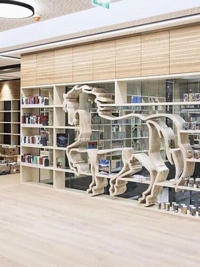 Heller Bibliotheksraum mit Bücherregalen und einer dekorativen Regalinstallation in Form eines Pferdes, in der Bibliothek Köflach. | © Schmiedbauer Katrin