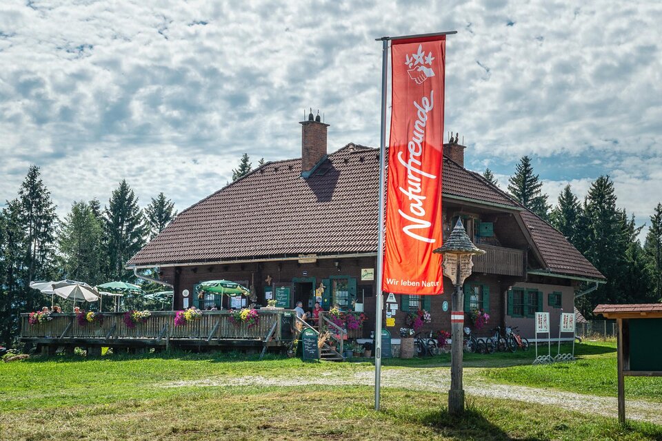 Ein großes Gebäude in der Natur mit einer Terrasse und vielen Pflanzen. Ein Banner mit der Aufschrift "Naturfreunde" ist sichtbar. | © Natufreunde / Doris List-Winder