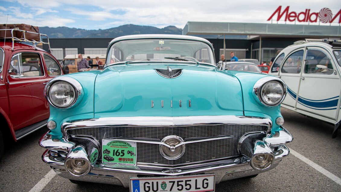 Ein klassisches Auto in leuchtendem Türkis mit glänzendem Chrom. Im Hintergrund sind weitere Oldtimer und ein klarer Himmel zu sehen. | © Ekaterina Paller