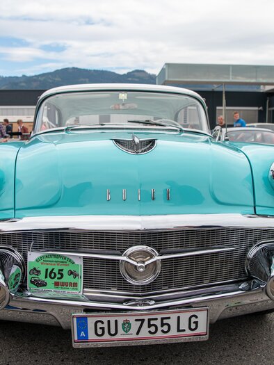 A classic car in bright turquoise with shiny chrome. In the background, there are more vintage cars and a clear sky. | © Ekaterina Paller