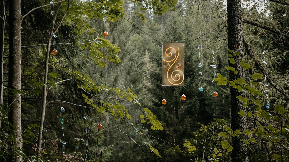 Ein mystischer Wald mit grünen Bäumen und einer goldenen Kunstinstallation in der Mitte. Bunte Objekte hängen zwischen den Bäumen und verleihen der Szene einen besonderen Charme. | © nicoleseiser.at
