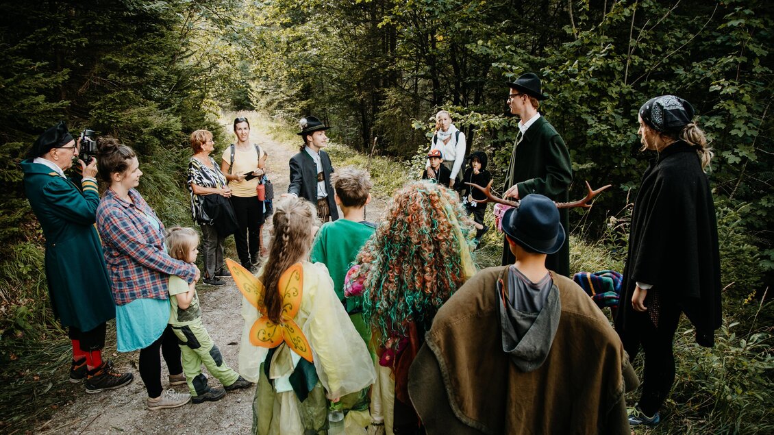 Eine Gruppe von Menschen in Kostümen steht auf einem Waldweg. Sie scheinen an einem Theaterstück oder einer Aufführung teilzunehmen. | © nicoleseiser.at