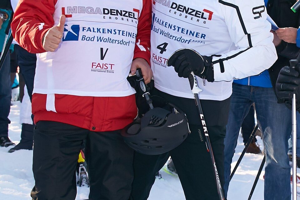 Zwei Skifahrer stehen nebeneinander im Schnee und posieren für ein Foto. Im Hintergrund sind weitere Personen und Berglandschaft zu sehen. | © Starpix/A. Tuma