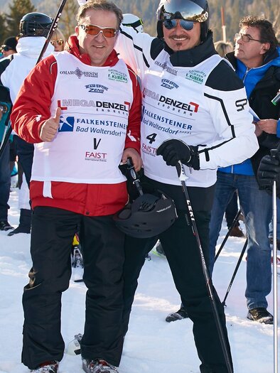 Zwei Skifahrer stehen nebeneinander im Schnee und posieren für ein Foto. Im Hintergrund sind weitere Personen und Berglandschaft zu sehen. | © Starpix/A. Tuma