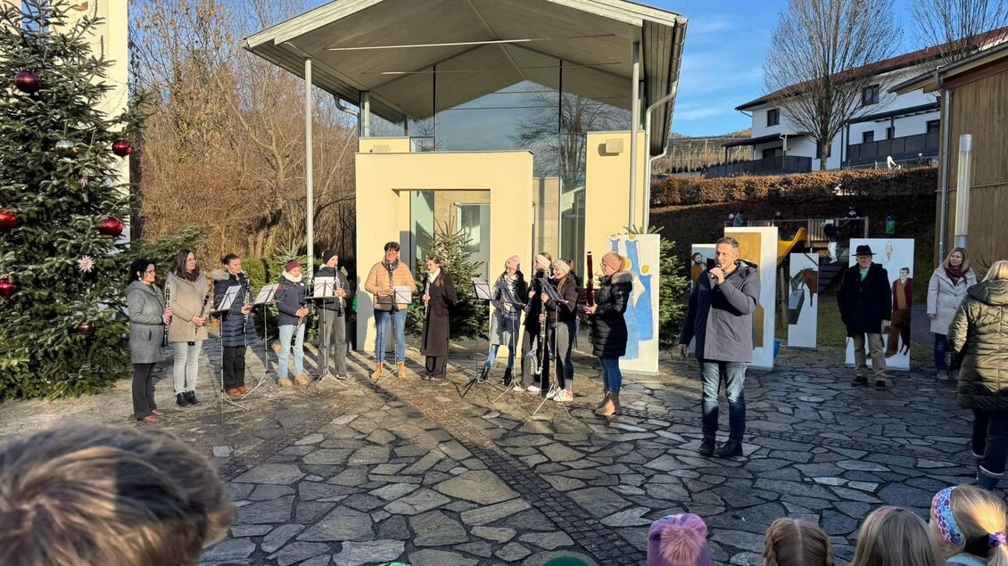Eine Gruppe von Menschen steht draußen und präsentiert etwas. Im Hintergrund sind Bäume und ein modernes Gebäude sowie Weihnachtsdekoration zu sehen. | © Gemeinde Floing