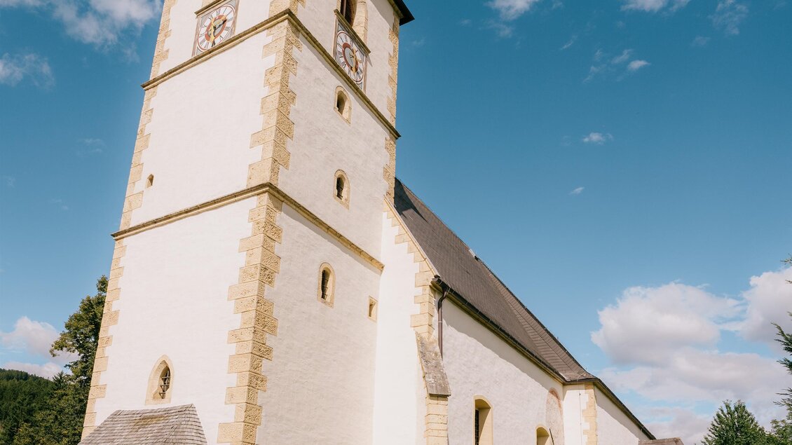 Eine schöne Kirche mit einem hohen Turm und einem klaren blauen Himmel. Spaziergänger genießen die ruhige Umgebung. | © Roman Königshofer