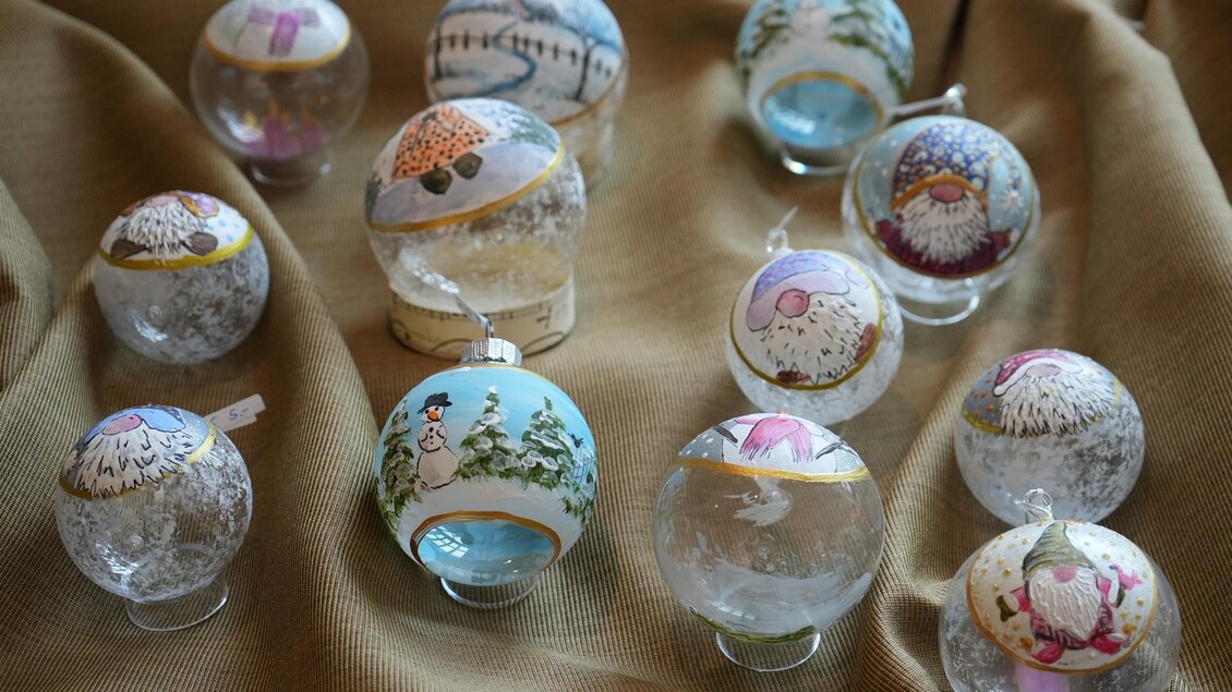 Eine Sammlung von handgefertigten Schneekugeln in verschiedenen Designs. Sie sind auf einem goldenen Stoff angeordnet und zeigen winterliche Szenen. | © Peter Haslebner