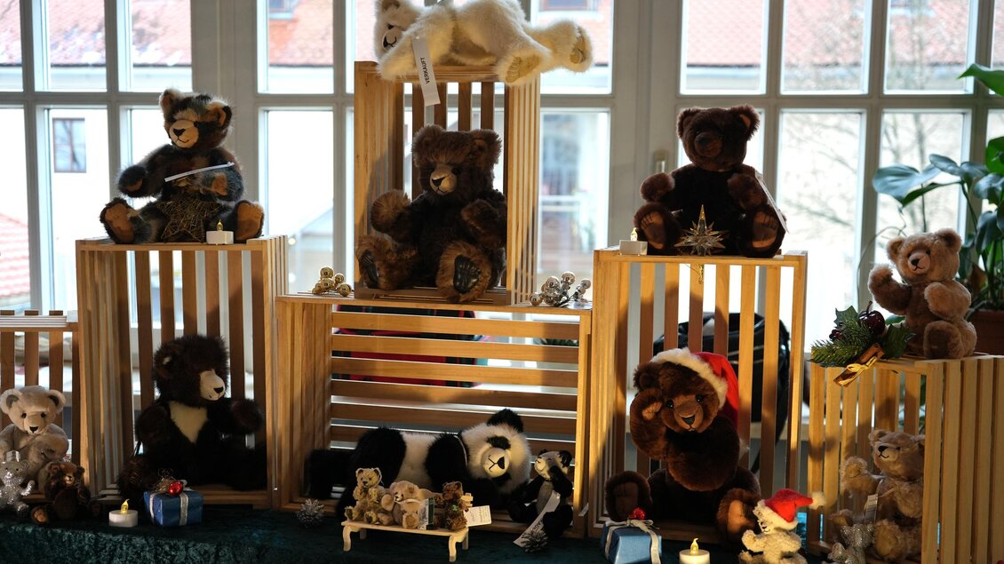 Eine Ausstellung von verschiedenen Plüschbären in Holzregalen. Die Bären sind in unterschiedlichen Posen und mit verschiedenen Accessoires dekoriert. | © Peter Haslebner