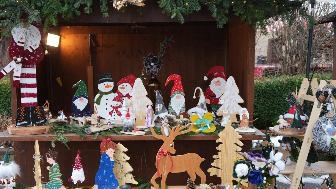 Ein festlich dekorierter Marktstand mit handgemachten Holzfiguren und Weihnachtsdekoration. Zu sehen sind Schneemänner, Weihnachtsmänner und verschiedene Tannenbäume. | © Peter Haslebner