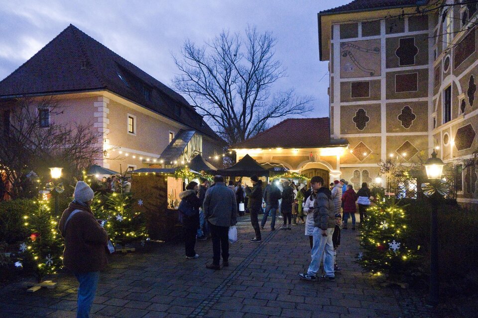 Ein einladender Weihnachtsmarkt mit festlich geschmückten Ständen und Lichtern. Die Atmosphäre ist lebhaft und festlich, während die Besucher die Stände erkunden. | © Peter Haslebner