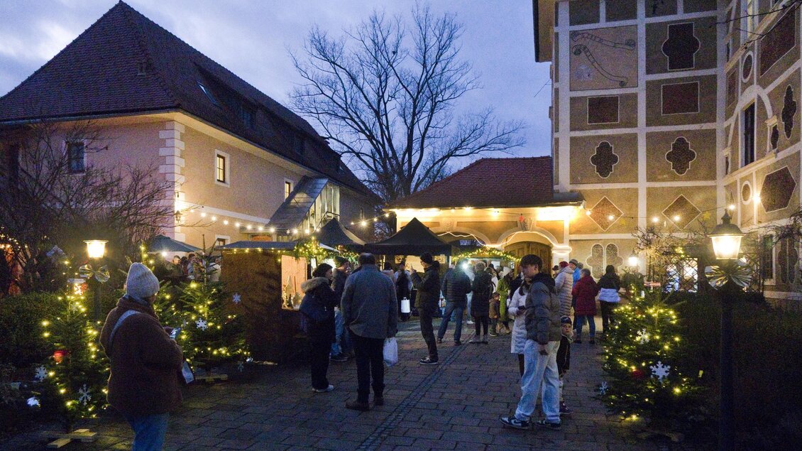 Ein einladender Weihnachtsmarkt mit festlich geschmückten Ständen und Lichtern. Die Atmosphäre ist lebhaft und festlich, während die Besucher die Stände erkunden. | © Peter Haslebner