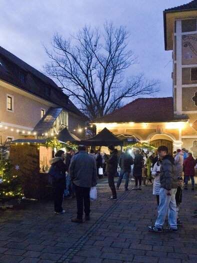 An inviting Christmas market with festively decorated stalls and lights. The atmosphere is lively and festive as visitors explore the stalls. | © Peter Haslebner