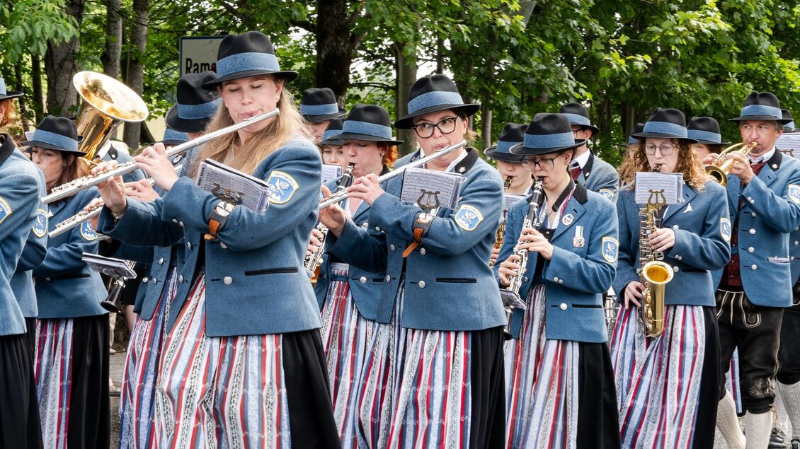 Eine Musikkapelle marschiert durch eine Straße. Die Musiker tragen traditionelle Kostüme und spielen verschiedene Instrumente.